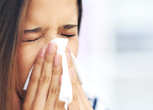 Photo of a woman with allergies blowing her nose into a tissue