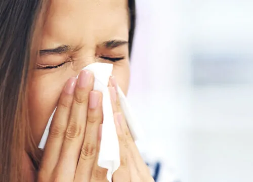 Photo of a woman with allergies blowing her nose into a tissue
